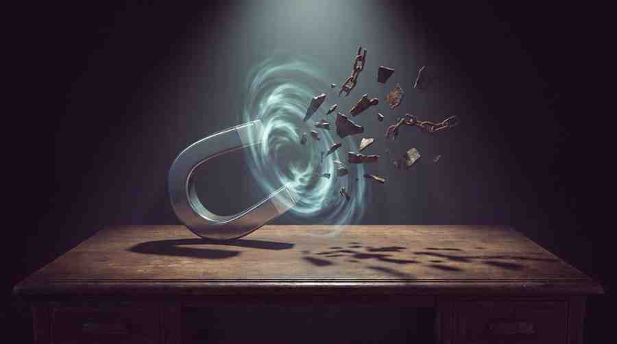 A sleek, shiny chrome horseshoe magnet sits on a dark rustic wooden table, magnetically pulling jagged old iron nails and broken chain links through the air from the right side under a dramatic top light.